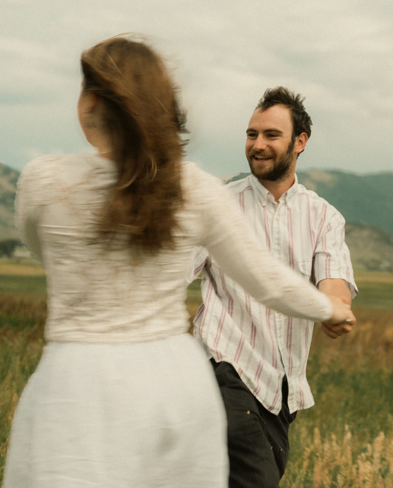 A couple dancing in tall grass with mountains behind them