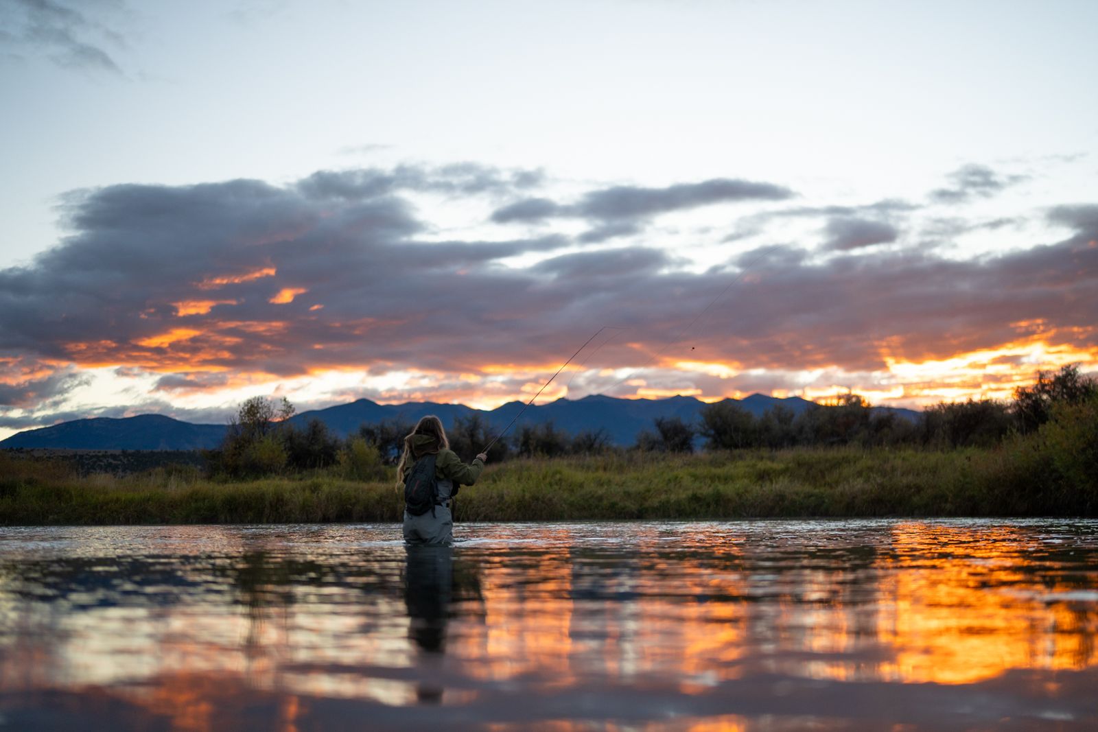 An angler casting at sunset, river reflecting the sky
